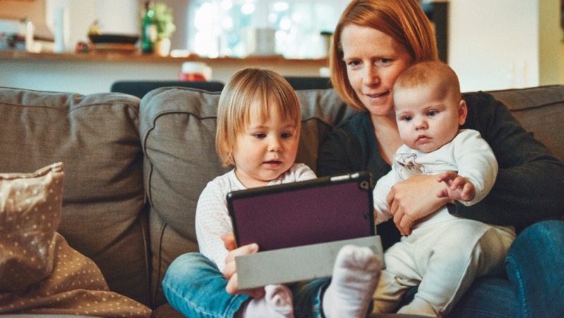 Woman with two young children sitting on a sofa looking at an iPad